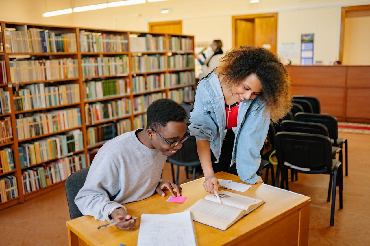Two students collaborating at a library table, engaged in study and learning with books.